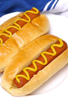 two hotdogs with mustard sitting on a white plate