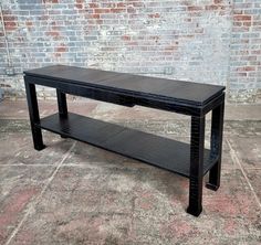 a black table sitting on top of a cement floor next to a brick wall with a wooden shelf underneath it