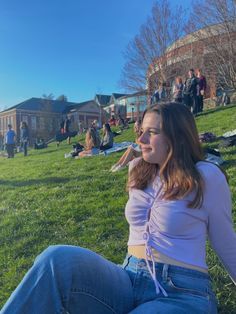 a woman sitting in the grass with her legs crossed and looking off to the side