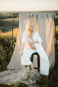 a woman sitting on top of a chair next to a white sheet in a field