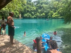 some people are swimming in the water and one is standing on a dock with a raft