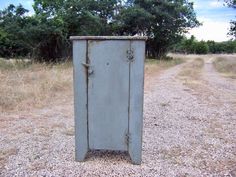 an old metal box sitting in the middle of a dirt road next to some trees