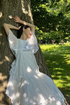 a woman in a white dress leaning against a tree