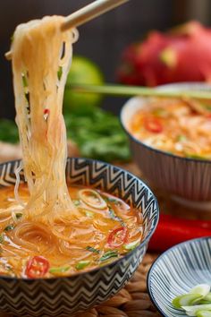 chopsticks lifting noodles from a bowl of soup with other bowls in the background