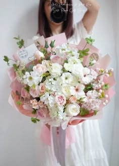 a woman holding a bouquet of white and pink flowers in front of her face while taking a selfie