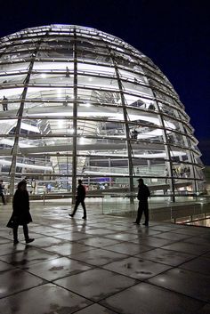 people are walking around in front of a large dome structure at night with lights shining on it