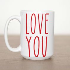 a white coffee mug with the words love you on it sitting on a wooden table