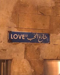 a blue street sign hanging from the side of a building in arabic writing on a stone wall