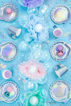 there are balloons, plates and other decorations on this blue tablecloth with pastel colors