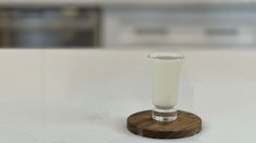 a shot glass sitting on top of a white counter next to a wooden stand with a small amount of liquid in it