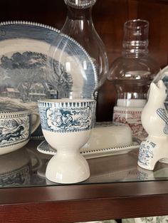 an assortment of china on display in a glass case with other dishes and vases behind it