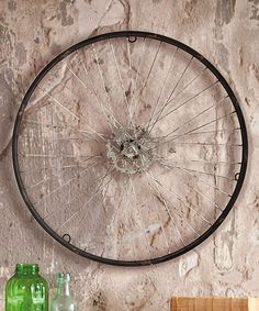 an old bicycle wheel hanging on the wall next to bottles and other items in front of it