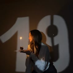 a woman holding a cake with a lit candle on it in front of a wall