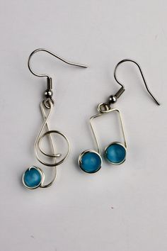 two earrings with musical notes and blue glass beads on the earwires, sitting on a white surface