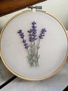 a close up of a embroidery on a table with a wooden frame and purple flowers