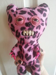 a hand holding a pink and black stuffed animal with big eyes on it's face