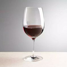 a wine glass filled with red wine on top of a wooden table next to a gray wall