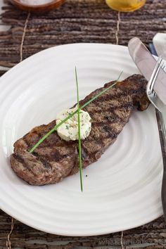 a piece of steak is sitting on a white plate next to a knife and fork