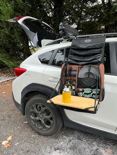 the back end of a white car with its trunk open and camping equipment in it