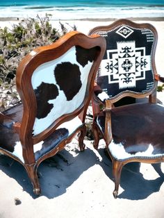 two wooden chairs with cow hide upholstered on the back are sitting in the sand at the beach