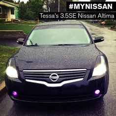 a black car parked in front of a house on a rainy day with purple lights