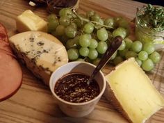 a wooden table topped with cheese, meat and grapes