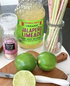 some limes are sitting on a cutting board next to other food and drink items