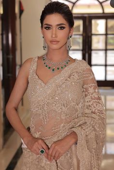 a woman in a beige sari and matching jewelry poses for the camera with her hands on her hips