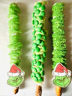 there are three candy sticks with green candies on them and one has an elf's hat