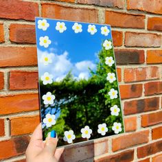 a person holding up a piece of paper with flowers on it in front of a brick wall