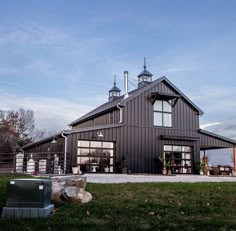 a black barn with two large windows on the front and side of it, surrounded by green grass