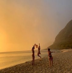 three people on the beach playing with a frisbee in front of some mountains