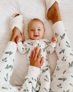 a baby laying on top of a white bed next to two women's feet