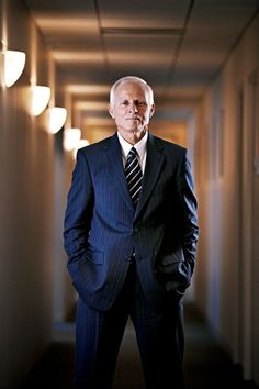 a man in a suit and tie is standing in an empty hallway with his hands in his pockets