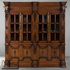 a large wooden cabinet with glass doors and carvings on the front, in an empty room