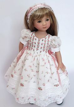 the doll is wearing a white dress with pink flowers on it's chest and headband