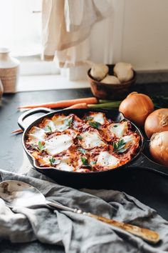 an iron skillet filled with food on top of a counter next to onions and carrots