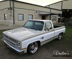 a white pickup truck parked in front of a building with grass and dirt on the ground