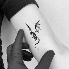 a person with a tattoo on their arm holding up a small black and white dragon