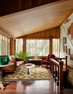 a living room with wood paneling and green pillows on the couches in front of large windows