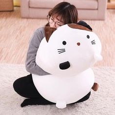 a woman sitting on the floor with a large white cat inflatable pillow behind her