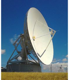 a large satellite dish sitting on top of a dry grass covered field under a blue sky