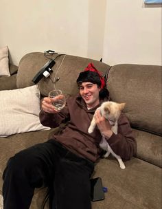 a man sitting on a couch with a cat in his lap holding a glass of wine