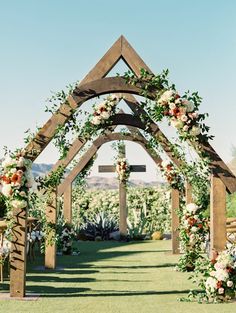 a wooden arch with flowers and greenery on the side is an outdoor wedding venue