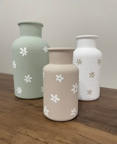 three vases sitting on top of a wooden table with white flowers painted on them