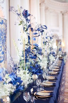 a long table is set with blue and white floral centerpieces, silverware, and place settings