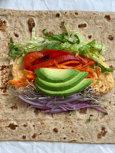 a tortilla filled with vegetables and sliced avocado on top of it