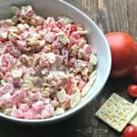 a bowl filled with diced meat next to tomatoes and crackers