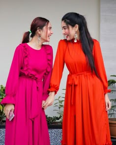 two women standing next to each other in bright colored dresses and smiling at each other