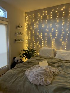 an unmade bed with white lights on the headboard and pillows in front of it